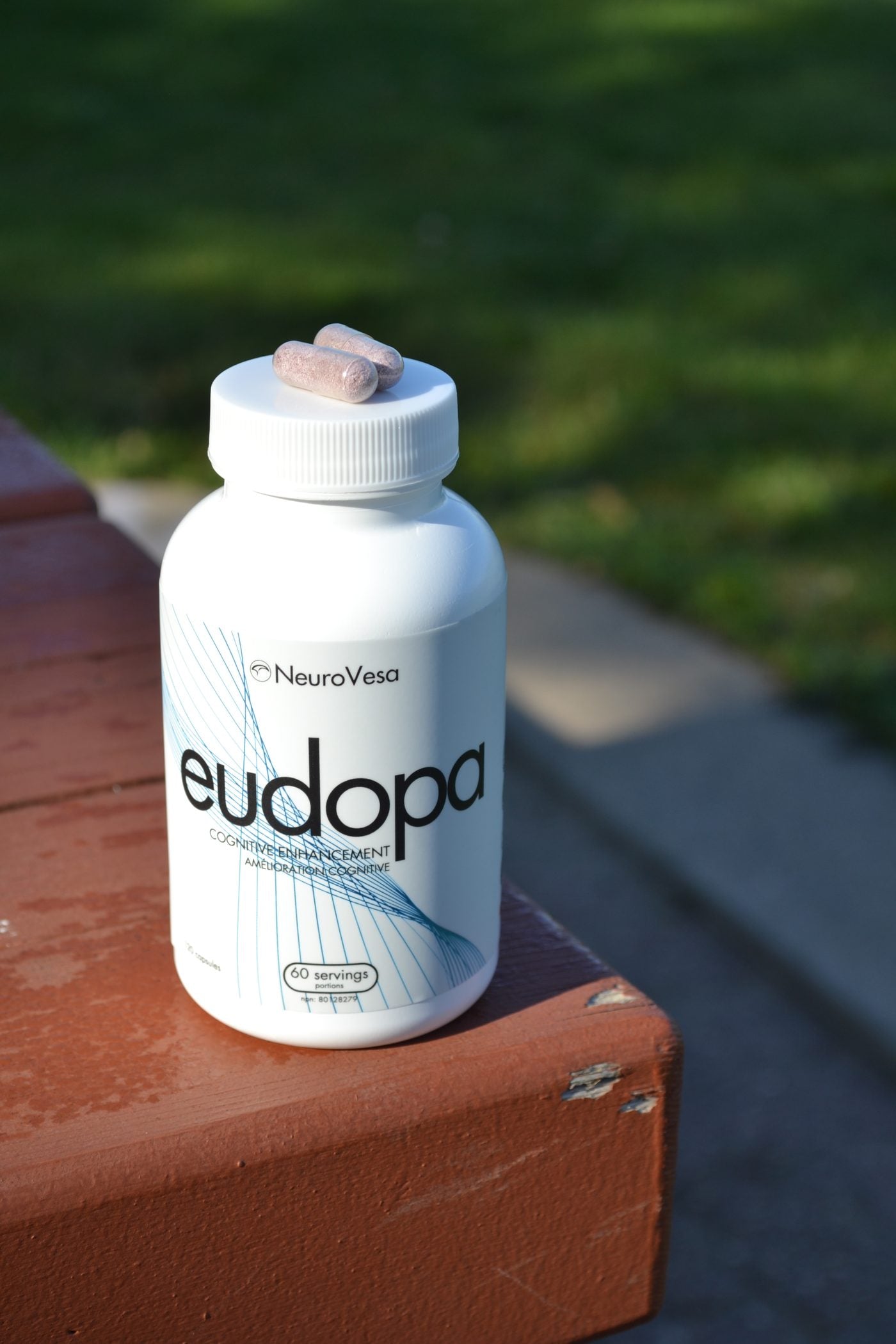 A bottle of eudopa on a bench outdoors with two capsules resting on the cap